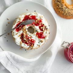 bagel with cream cheese and raspberry jam on a white plate