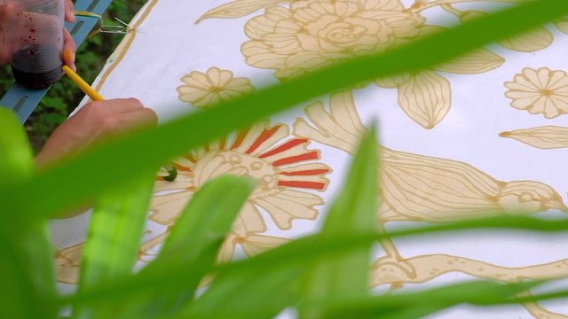 Close up of hand drawing traditional batik pattern with hot wax using canting tool.
