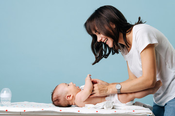 Young beautiful mom changes baby's diaper and smiles at him