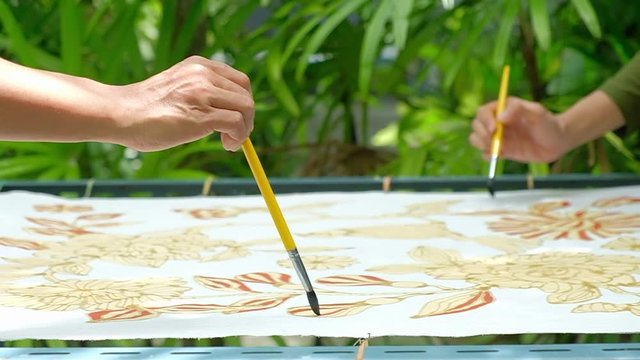 Close up of hand drawing traditional batik pattern with hot wax using canting tool.