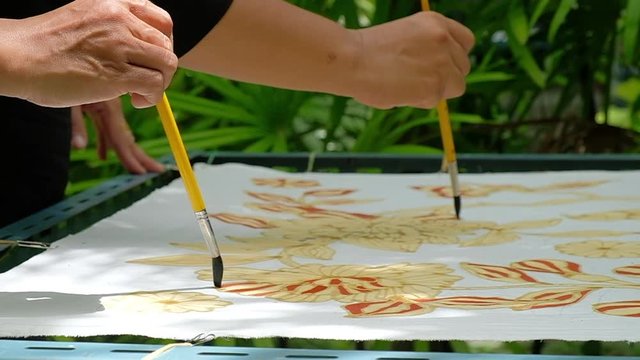 Close up of hand drawing traditional batik pattern with hot wax using canting tool.