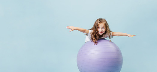 Curly-haired funny girl plays on a gymnastic ball