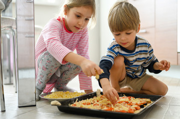 Obraz na płótnie Canvas happy family make food at home. little kids son and daughter helps his mother cooking pizza in the kitchen. concept pastimes of isolation time in quarantine mode during coronavirus covid-19