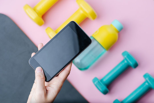 Hand taking a picture of dumbbells and bottle of water lying on a mat. Top view.