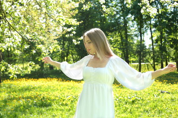Naklejka na ściany i meble Happy blonde woman on a background of blooming spring garden with her hands raised to the sky