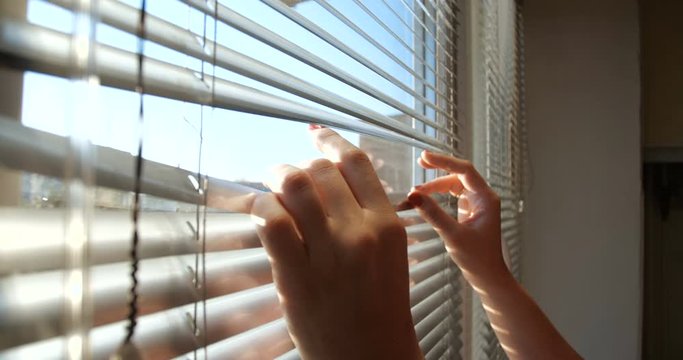 Close up shot from indoors of hands of woman pushing  blinds at window at home. Looking fearfully outside because afraid of germs. The concept of quarantine,  self-isolation 4kslow motion