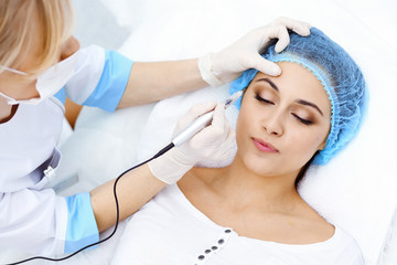 Naklejka premium Professional beautician doing eyebrow tattoo at woman face. Permanent brow makeup in beauty salon, closeup. Cosmetology treatment