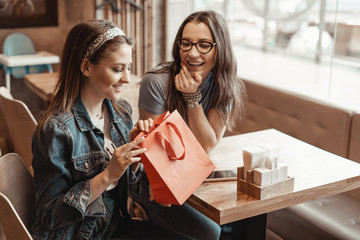 Trade, buyers. Two beautiful girls make purchases in a shopping center, go shopping. Gift for the holiday. The girl gives a gift to her friend. The joy of consumption.
