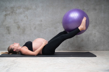 Portrait of pretty pregnant woman exercises with fitball in the gym. Working out and fitness,...