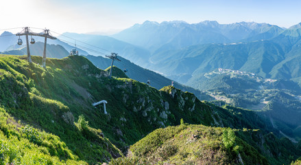 Panoramic view of the sunset in summer from the top of the Aibga range to the ski resort Rosa Khutor. The cable car is illuminated by the sunset. Beautiful sunset in mountains