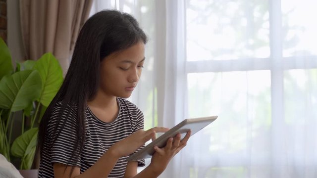 asian teenage girl using mobile tablet while sitting on the bed