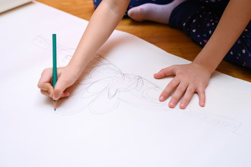 kids hobby. a little six year old child girl draws with a pencil on paper sitting on the floor at home. the concept of home exercises during the coronavirus covid-19 quarantine