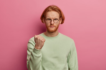 Outraged bearded man with bob hairstyle, clenches fist, frowns from insult and displeasure,...