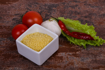 Raw couscous in the bowl served salad leaves, tomato and pepper