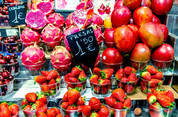 Fresh strawberries, red mango and pink dragon fruits or pitaya or pitahaya in plastic glasses in the Boqueria market, Barcelona, Spain