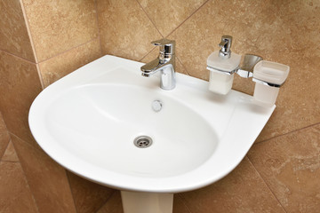 New white sink and liquid soap on a background of a brown wall in the bathroom.