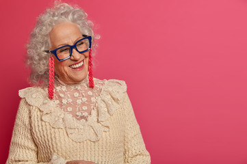 Close up portrait of happy wrinkled granny looks aside with beaming smile, enjoys pleasant talk...