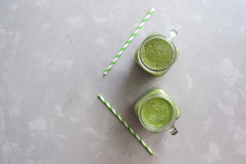 Top view on two glasses of green smoothie and green tubules on a gray concrete background. Place for text. Vegan food. Vitamin snack