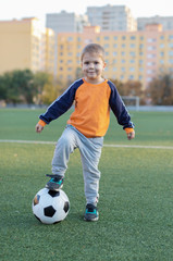 little boy plays football on the football field gives a pass hits the ball runs across the field and scores a goal sports child soccer player trains in the fresh air