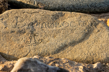 Vladivostok, Russia - March, 21, 2020: A stone with the word Vladivostok embossed on it, an anchor and flying gulls lying on the Tokarevskaya Spit leading to the  Tokarevsky Lighthouse in Vladivostok.