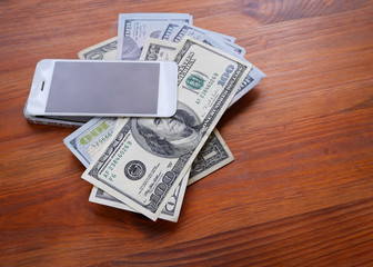 Mobile phone and money on a wooden background. The concept of making money using a smartphone. Pile of earned money using your phone.