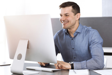 Businessman working with computer in modern sunny office. Headshot of male entrepreneur or company director at workplace. Business concept