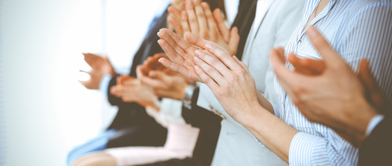 Obraz premium Business people clapping and applause at meeting or conference, close-up of hands. Group of unknown businessmen and women in modern white office. Success teamwork or corporate coaching concept