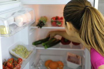 Back view of young woman searching for healthy food in the fridge