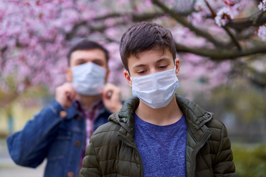 Father And Son With A Face Mask Are In The City Outdoor, Blooming Trees, Spring Season, Flowering Time - Concept Of Allergies And Health Protection From Dusty Air