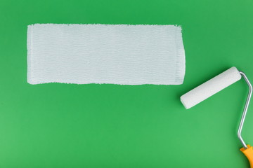painting roller and strip of white paint on green background