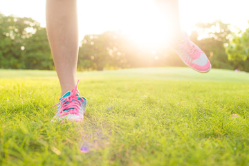 Foot of sport women running on green grass field in oark with sun light