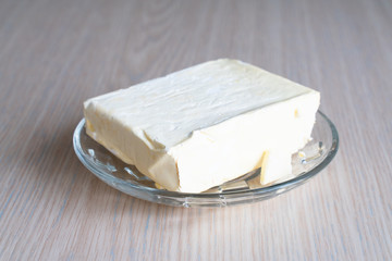 a briquette of butter on a glass plate on a wooden table close up