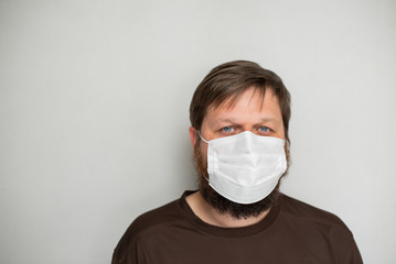 COVID-19 Pandemic Coronavirus. Portrait of a man with a beard in a white mask on a light background