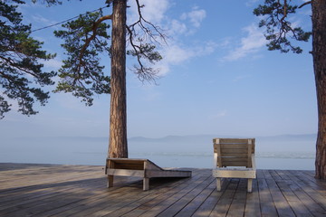 Spring morning, by the lake on which the snow melts, there are two empty deck chairs, pine trees grow nearby, there are no people around. The concept of loneliness, relaxation