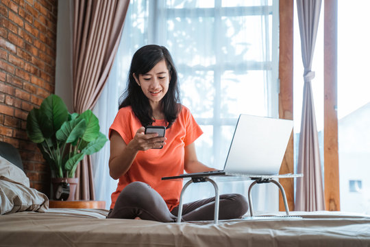 asian woman working from home sitting on the bed