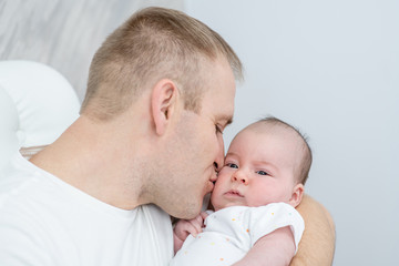 Happy young father hugs and kisses his sweet adorable newborn son
