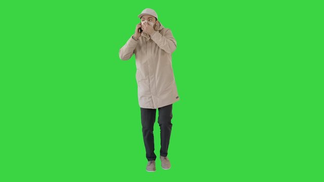 Casual man in outdoor clothes and medical mask walking and talking on the phone on a Green Screen, Chroma Key.