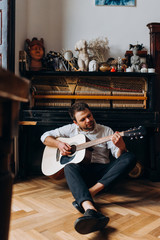 A man sits on the floor and plays guitar. Guy with guitar in his hands.