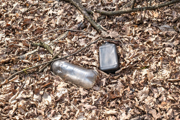 A dirty plastic and glass bottle left in the autumn forest. Plastic waste in the environment.