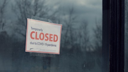 FIXED view of a Temporary closed due COVID-19 pandemic sign hanging on a window. Coronavirus pandemic, small business shutdown - obrazy, fototapety, plakaty