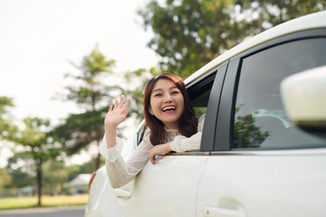 Attractive smiling woman waving her hand from the car window.