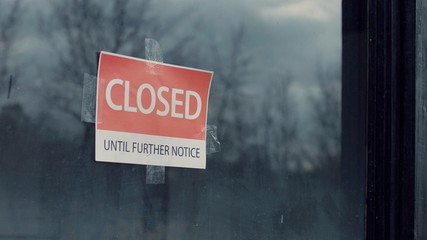 FIXED view of a sign saying Closed until further notice taped to a window. Coronavirus pandemic,...