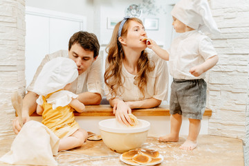 Charming two-year-old boy gives his mother a try to bake pancakes during family cooking with dad...