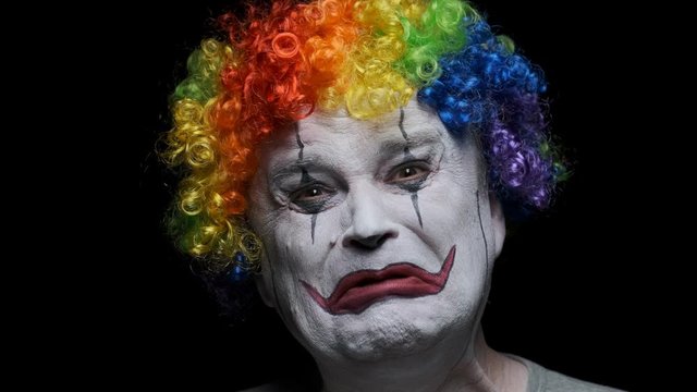Portrait of sad clown man crying on black background.