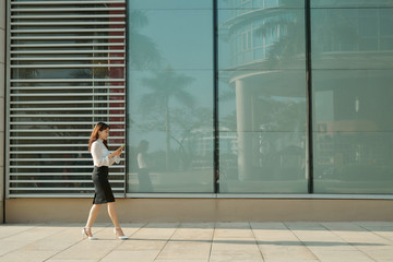Fototapeta na wymiar Full length side portrait of a young woman walking and sending text message on cell phone