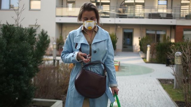 Young blonde woman in a protective mask returns home with a package of products from the store, takes out the apartment key from her pocket. Cowid-19 coronovirus epidemic, quarantine