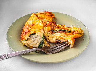Hot breakfast consisting of omelet with spinach and butter on a round ceramic plate