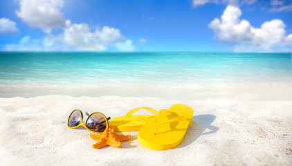 Concept of summer beach holiday. Beach accessories - sunglasses, starfish, yellow flip-flops on...