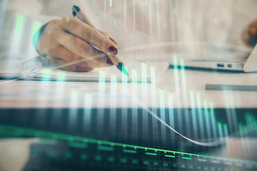 Double exposure of woman's hands making notes with forex graph hologram. Concept technical analysis.