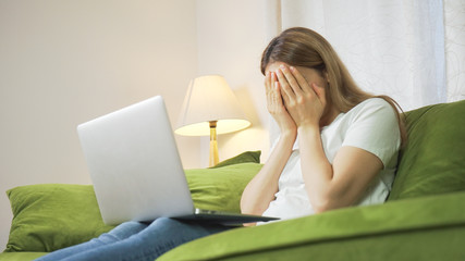 Young girl crying on couch having a facetime video call. Stressed woman on sofa working from home. Sad female student in crisis feeling depressed.  